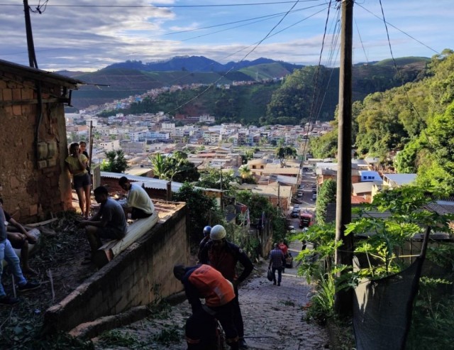 Bombeiros e moradores em rua de Ibatiba durante atendimento após queda de eucalipto sobre residências.