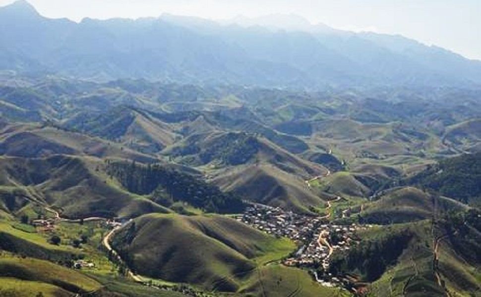 Fotografia aérea das montanhas da região do Caparaó, mostrando o relevo acidentado com plantações de café e a cidade de Divino de São Lourenço ao pé das montanhas sob céu claro.