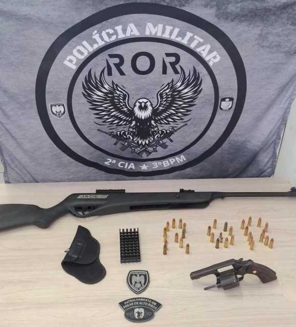 Armas e munições apreendidas pela Polícia Militar, incluindo revólver, munições e espingarda de pressão, expostas sobre uma mesa durante ocorrência em Divino de São Lourenço.