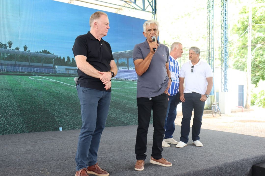 Governador do Espírito Santo acompanha pronunciamento durante solenidade em Muniz Freire, com autoridades estaduais e municipais no palco, tendo ao fundo imagem ilustrativa do projeto do Estádio José Ibrahim Nicolau.