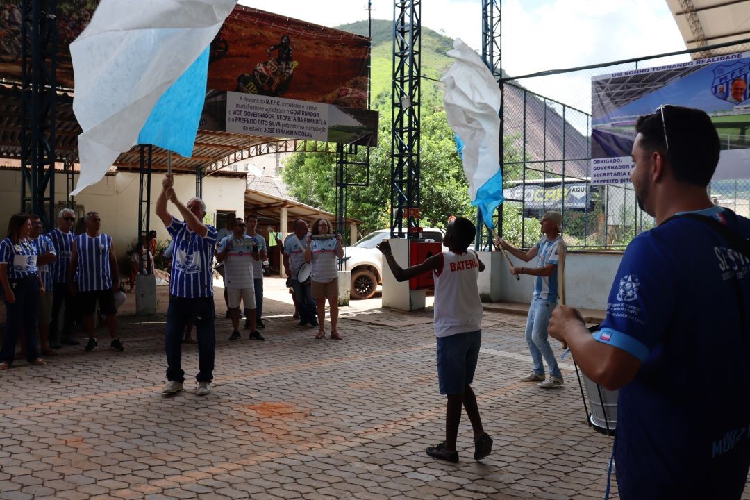Torcida do Muniz Freire FC se manifesta com bandeiras, instrumentos e charanga durante evento oficial, comemorando o anúncio da reforma do Estádio José Ibrahim Nicolau, no município de Muniz Freire.