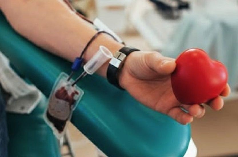 Braço de um doador durante coleta de sangue, segurando um objeto em formato de coração vermelho, simbolizando solidariedade e doação de sangue.