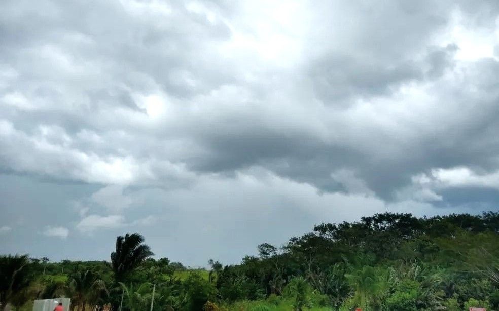 Paisagem da região do Caparaó com céu densamente nublado, nuvens cinzas carregadas sobre vegetação típica de mata atlântica e palmeiras.