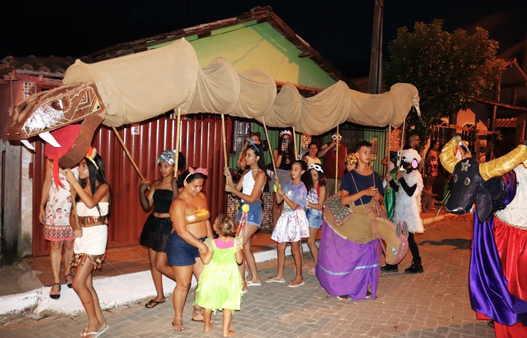 Integrantes do Bloco Criaturas da Floresta desfilam à noite pelas ruas de Patrimônio da Penha, carregando uma grande cobra cenográfica e personagens da cultura popular durante o Carnaval 2026.