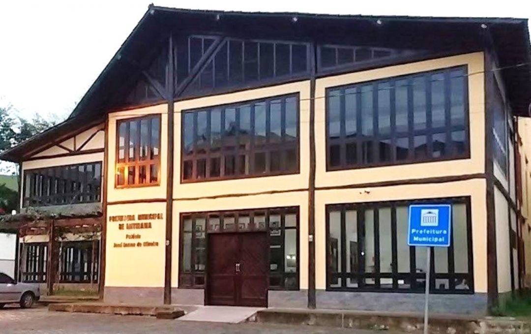 Fachada da Prefeitura de Ibitirama, prédio de dois andares com estrutura em madeira aparente e grandes janelas de vidro, com placa indicativa de “Prefeitura Municipal” na área externa.