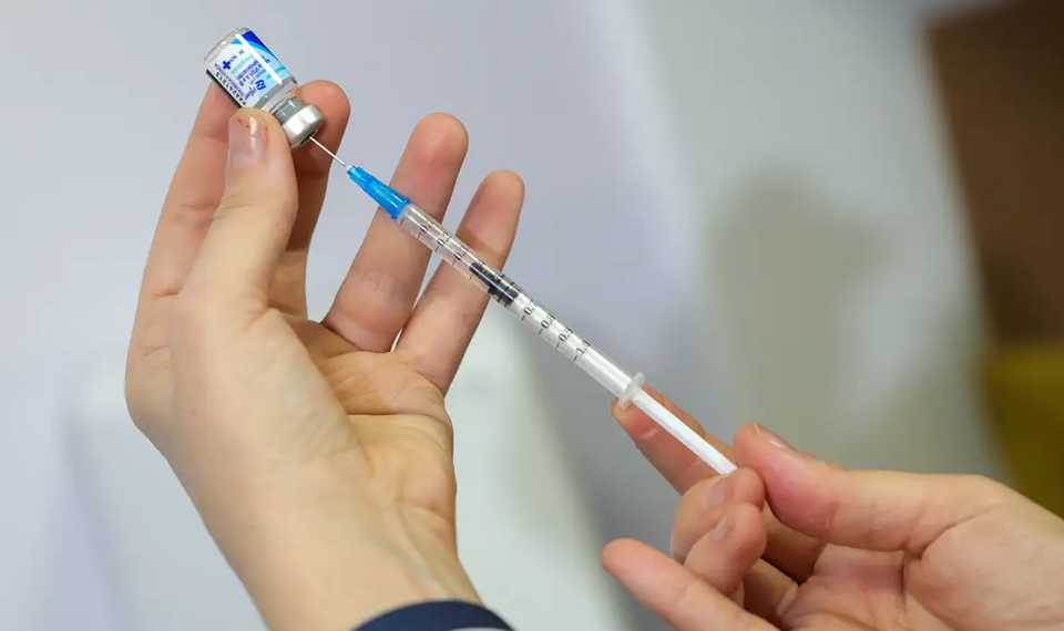 Profissional de saúde segura frasco de vacina e prepara seringa para aplicação intramuscular, ilustrando a imunização contra o Vírus Sincicial Respiratório (VSR).