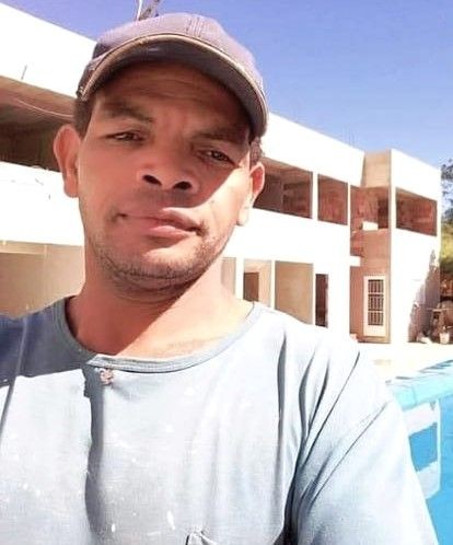 Foto da vítima de homicídio no bairro Boa Esperança, em Ibatiba, tendo um prédio ao fundo e o céu bem azul.