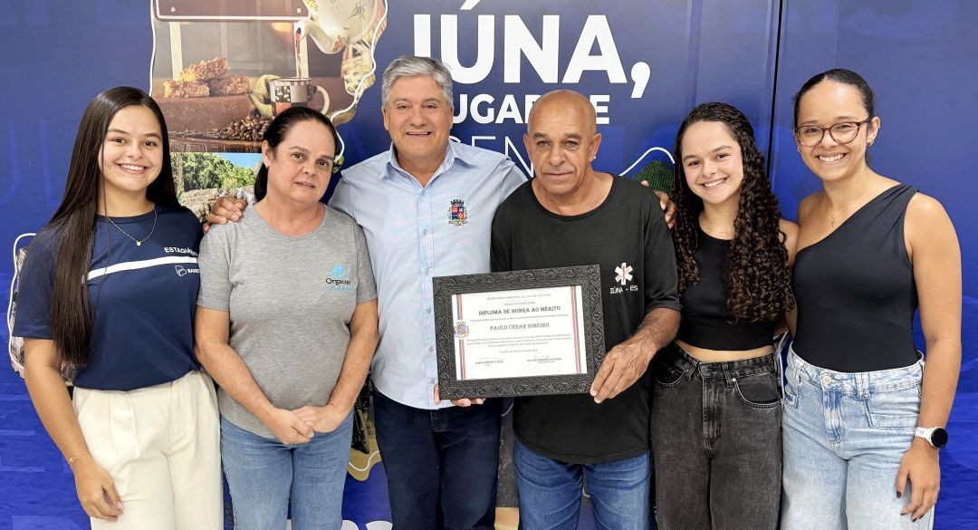 Motorista Paulo Cézar Ribeiro recebe homenagem acompanhado do prefeito, familiares e representantes da Secretaria de Saúde, segurando o diploma em cerimônia oficial em Iúna.