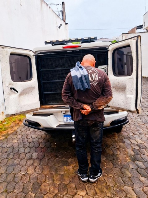 Homem com as mãos para trás sendo conduzido por policiais militares para viatura durante cumprimento de mandado de prisão em Guaçuí.