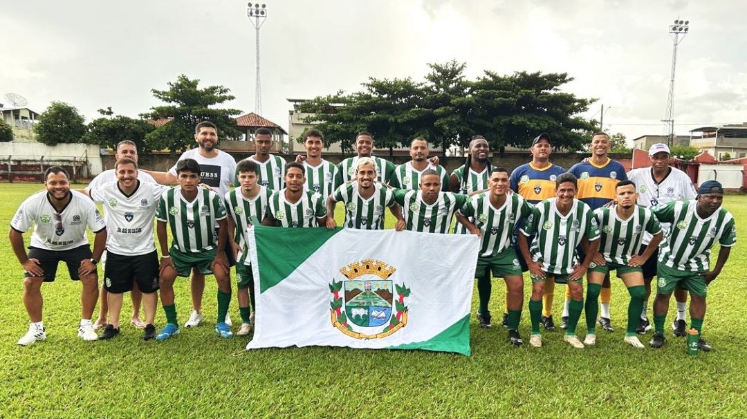 Elenco da equipe de São José do Calçado reunido antes de partida da Copa Sesport, tendo ao fundo torres de iluminação do campo, casas e o céu nublado.