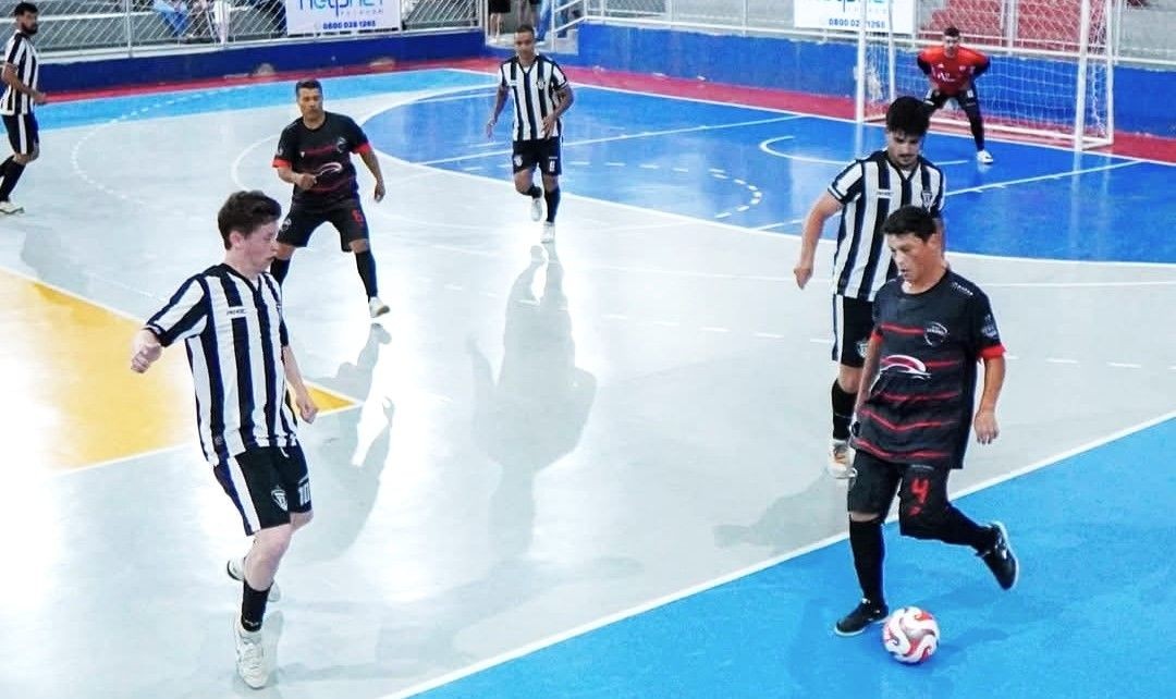 Lance de ataque durante a rodada de quarta-feira. Um jogador de preto conduz a bola pela ala direita enquanto o adversário de uniforme listrado tenta o desarme. Ao fundo, o goleiro se posiciona para a defesa.
