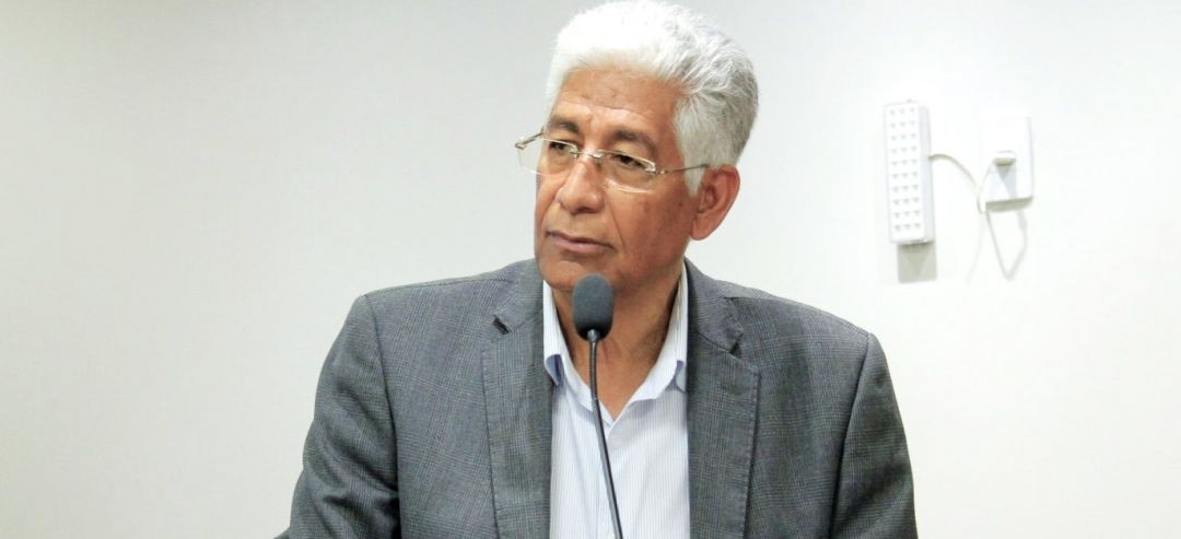 Prefeito Luis Pancoti falando em um microfone, vestindo terno cinza e camisa clara, tendo ao fundo uma parede branca.