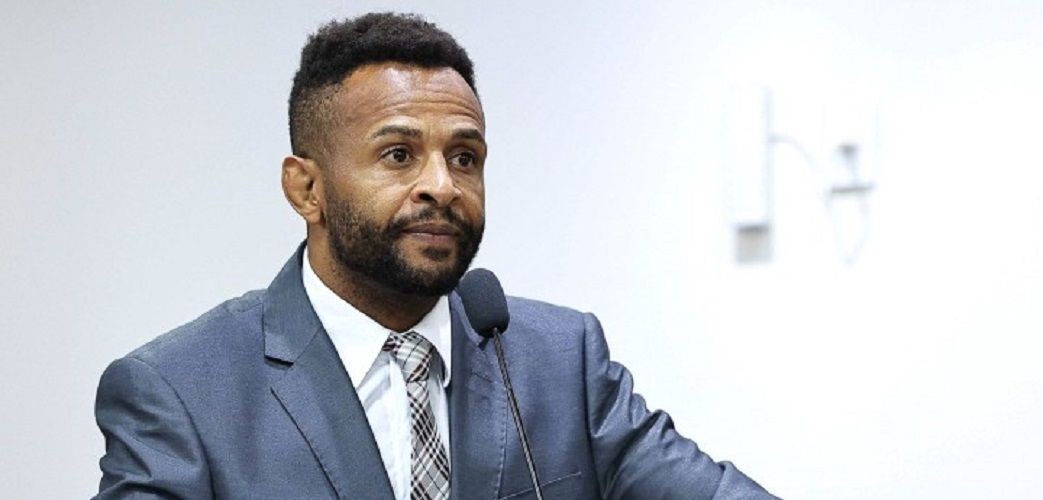 Foto do vereador Professor Wesley, de Ibatiba, falando ao microfone, em um sessão da Câmara Municipal, com fundo branco.