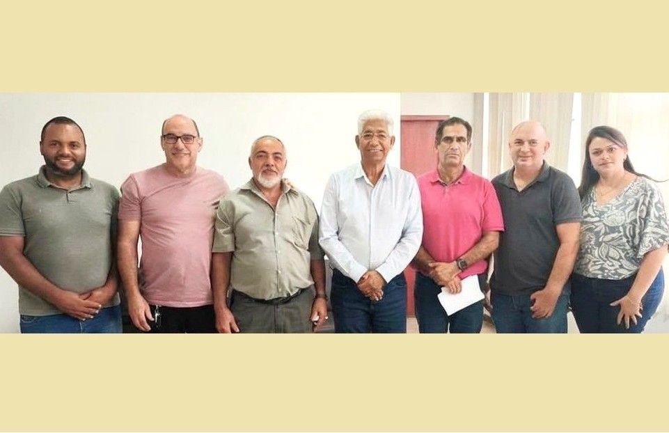 Grupo de pessoas, incluindo o prefeito de Ibatiba, Luis Pancoti, e representantes do sindicato e da administração municipal, posando lado a lado em ambiente interno durante reunião sobre reajuste salarial de servidores em Ibatiba.