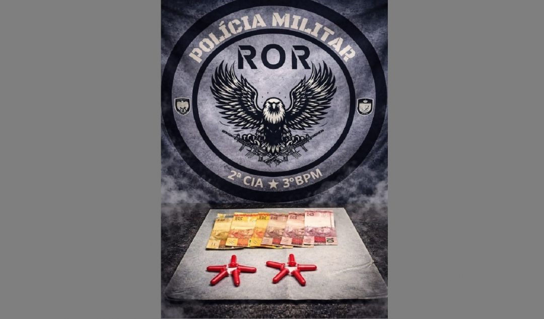 Imagem mostra dinheiro em cédulas e pinos vermelhos contendo substância semelhante à cocaína dispostos sobre uma superfície, com o emblema da Polícia Militar ao fundo.