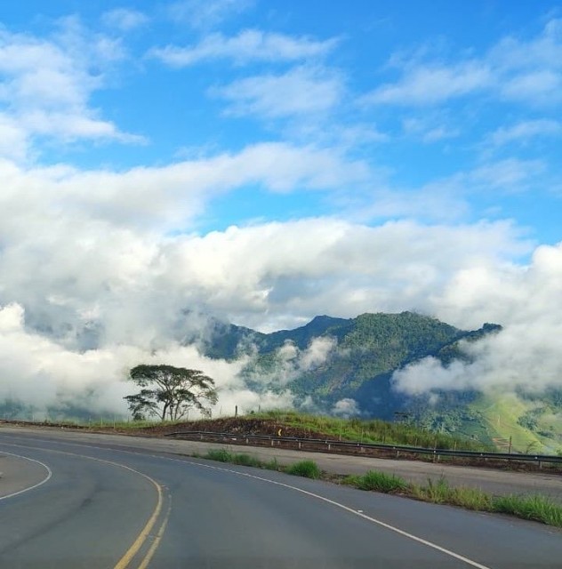 Rodovia sinuosa em região montanhosa do Caparaó capixaba, com céu parcialmente nublado e neblina sobre as montanhas ao fundo.