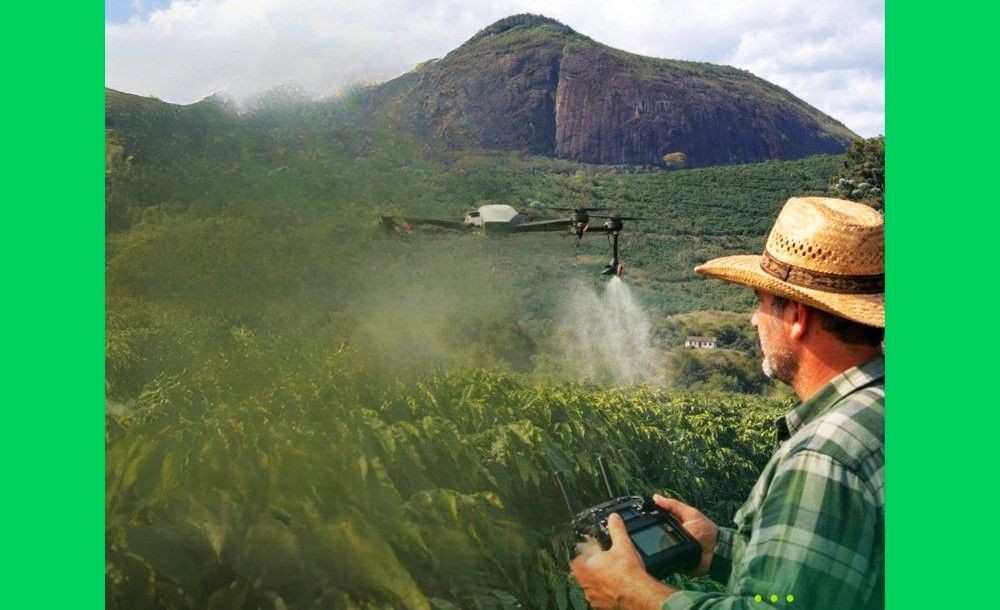 Homem com chapéu de palha opera controle remoto de drone que sobrevoa e aplica insumos em lavoura de café em Irupi, com montanhas ao fundo.