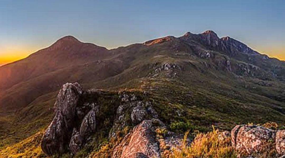 Paisagem da Serra do Caparaó, com formações rochosas e vegetação, iluminadas pela luz do pôr do sol.