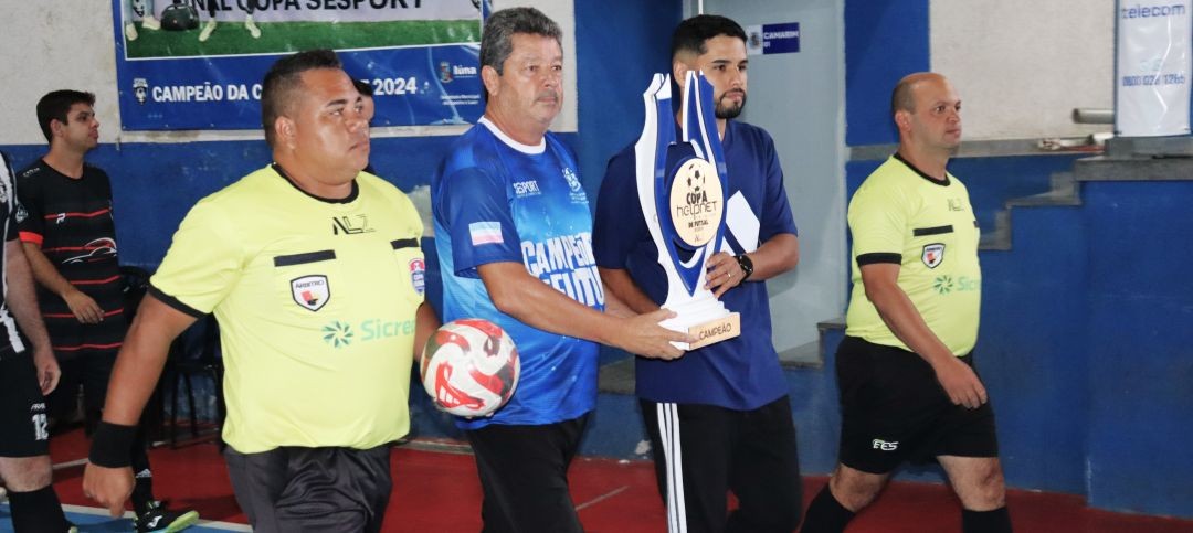 Árbitros, o secretário de Esportes Zizinho e Mateus Alvarez, da ALZ, entram em quadra carregando o troféu da final da Copa Helpnet Telecom de Futsal, antes da decisão em Iúna.