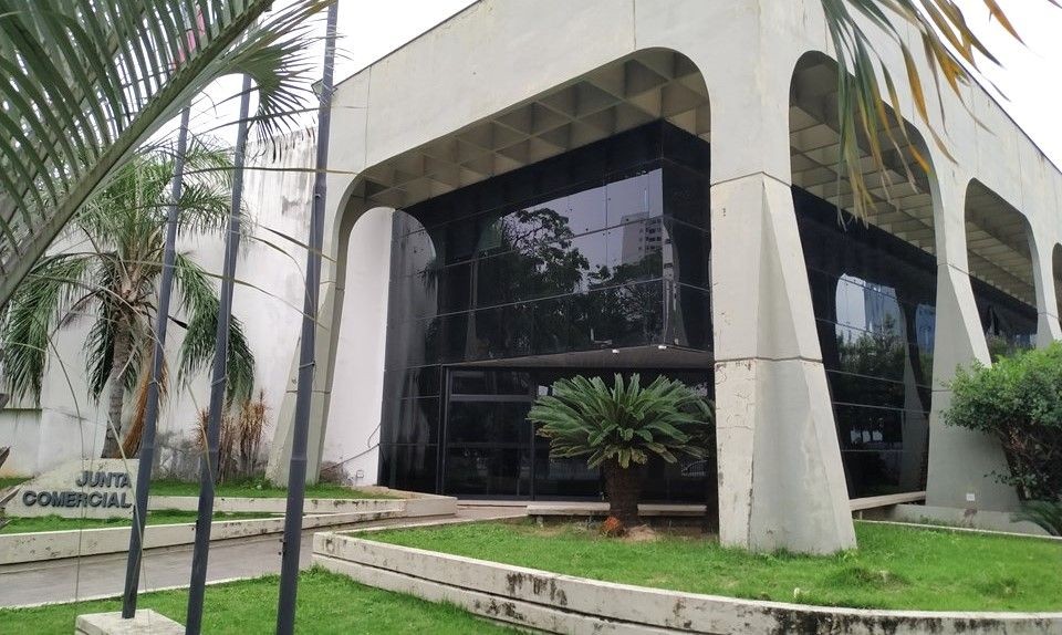 Fachada da Junta Comercial do Estado do Espírito Santo (Jucees), com estrutura em concreto, vidro escuro e área verde ao redor da entrada principal.