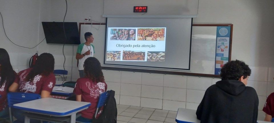 Aluno apresenta trabalho sobre povos indígenas em sala de aula durante workshop em escola estadual de Guaçuí.