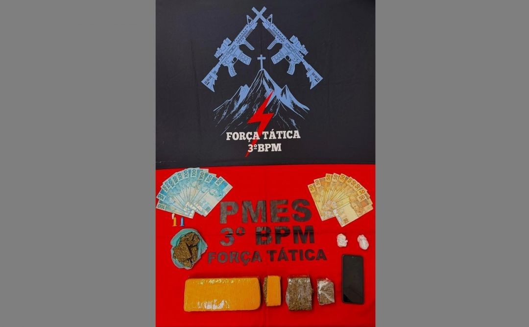 Mesa com materiais apreendidos pela Polícia Militar, incluindo porções de maconha e cocaína, dinheiro em espécie, celular e identificação da Força Tática do 3º BPM ao fundo.
