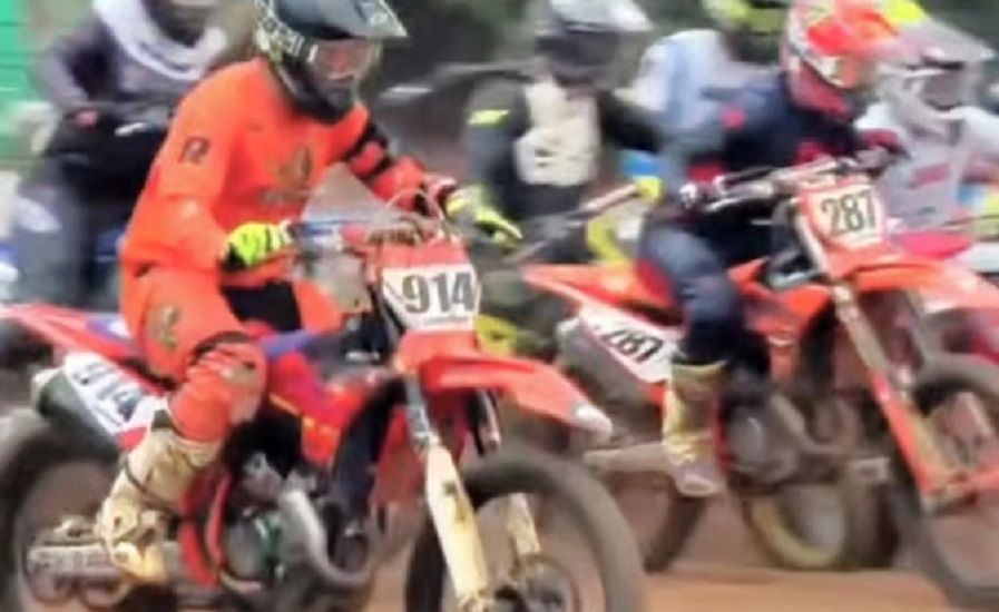 Pilotos de motocross participam de corrida em pista de terra, no momento da largada em grupo durante competição.