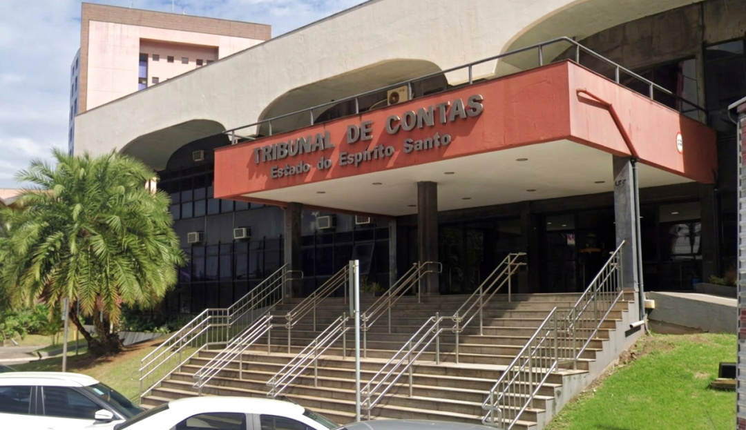 Uma fotografia da fachada do edifício do Tribunal de Contas do Estado do Espírito Santo (TCE-ES), localizado em Vitória. A imagem mostra a entrada principal, com uma escadaria de acesso de vários lances e corrimãos metálicos. Acima da escadaria, há uma cobertura sobressalente em tons de vermelho terracota, onde se lê a inscrição 