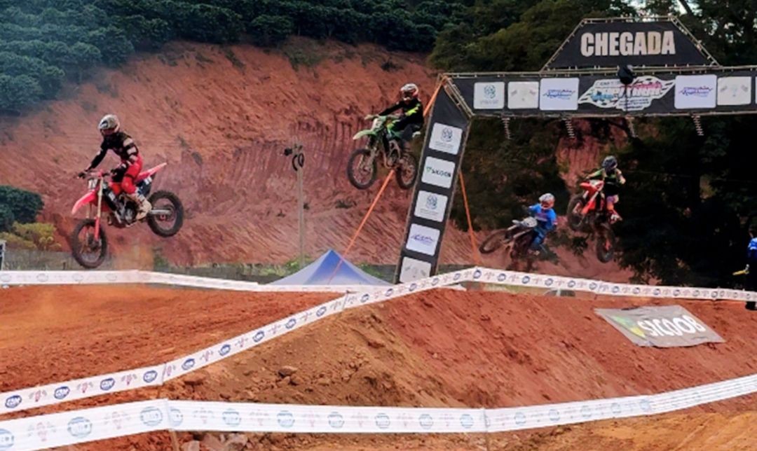 Pilotos realizando saltos com suas motos sob o pórtico de 