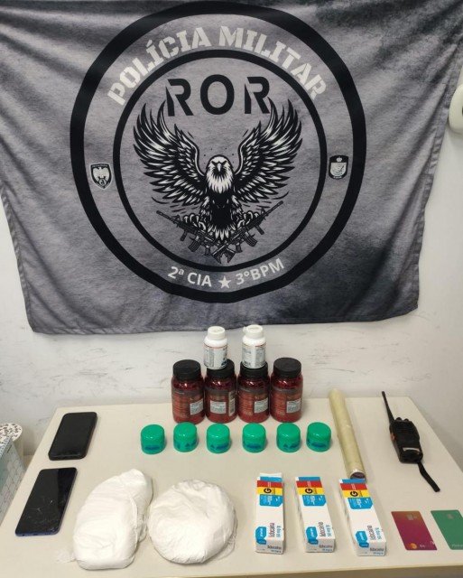 Imagem mostra mesa com materiais apreendidos pela Polícia Militar em Guaçuí, incluindo porções de cocaína, substâncias para preparo da droga, celulares, rádio comunicador e cartões bancários.