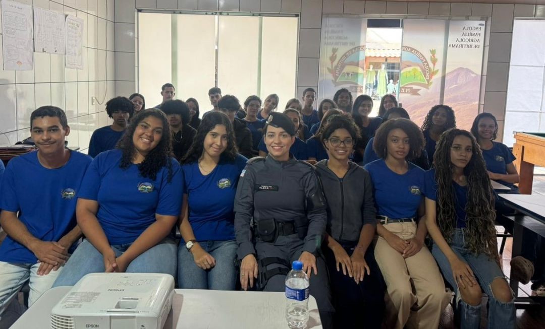 Policial militar uniformizada ao lado de estudantes dentro de sala de aula durante palestra educativa em escola de São José do Caparaó, em Ibitirama.