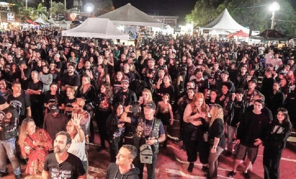 Fotografia noturna de plano aberto mostrando uma grande multidão reunida em frente a um palco (não visível). As pessoas, em sua maioria vestindo roupas pretas e coletes de motociclista, ocupam a área central do evento. Ao fundo, veem-se tendas brancas e a iluminação pública do Parque de Exposições de Iúna.