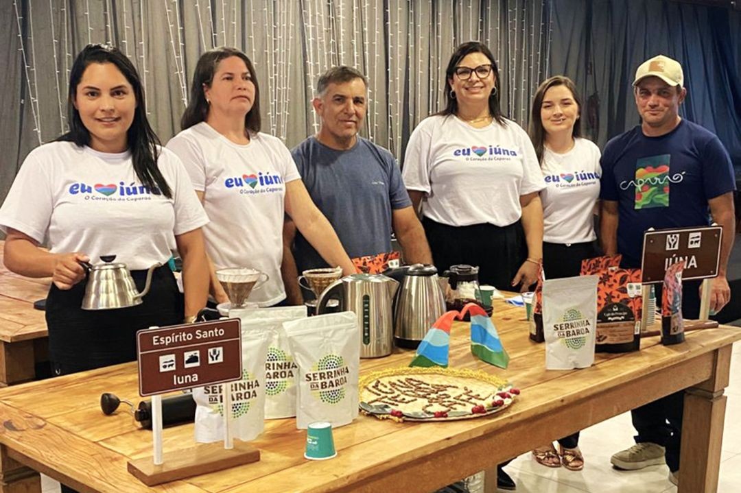 Grupo de seis pessoas posa atrás de uma mesa de madeira. Na mesa, há pacotes de 