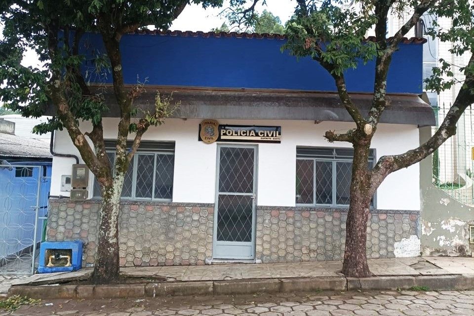 Fachada da Delegacia de Polícia Civil de Irupi, com porta central, janelas laterais e árvores na calçada em frente ao prédio.