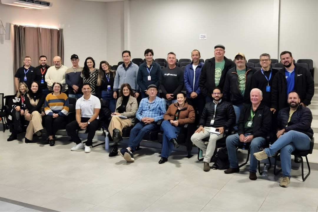 Foto em plano médio e ambiente fechado mostra o grupo de participantes do primeiro encontro do Projeto Governança Sem Fronteiras de 2026 reunido no auditório Francimar Carlos Pinheiro, em Pedra Menina. Ao todo, 26 pessoas entre homens e mulheres posam para o registro oficial. Na fileira da frente, parte do grupo está sentada em poltronas escuras de auditório, enquanto os demais participantes estão de pé logo atrás, posicionados em frente às fileiras de assentos vazios ao fundo. O grupo veste trajes casuais e profissionais; dois homens ao fundo vestem camisetas verdes com o logotipo do movimento territorial. A iluminação é clara e uniforme, sobre o piso de cerâmica cinza claro.