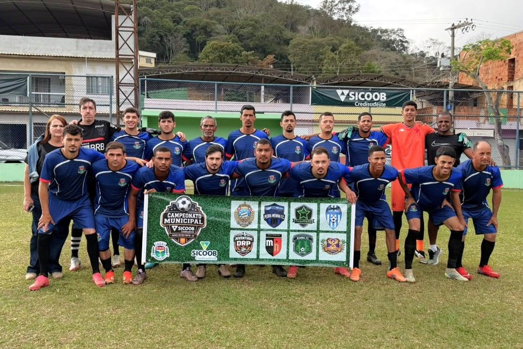 Equipe do Pedra Menina FC posa para foto antes da estreia no Campeonato Municipal de Dores do Rio Preto 2026, em campo de futebol, com atletas, comissão técnica e banner oficial da competição.