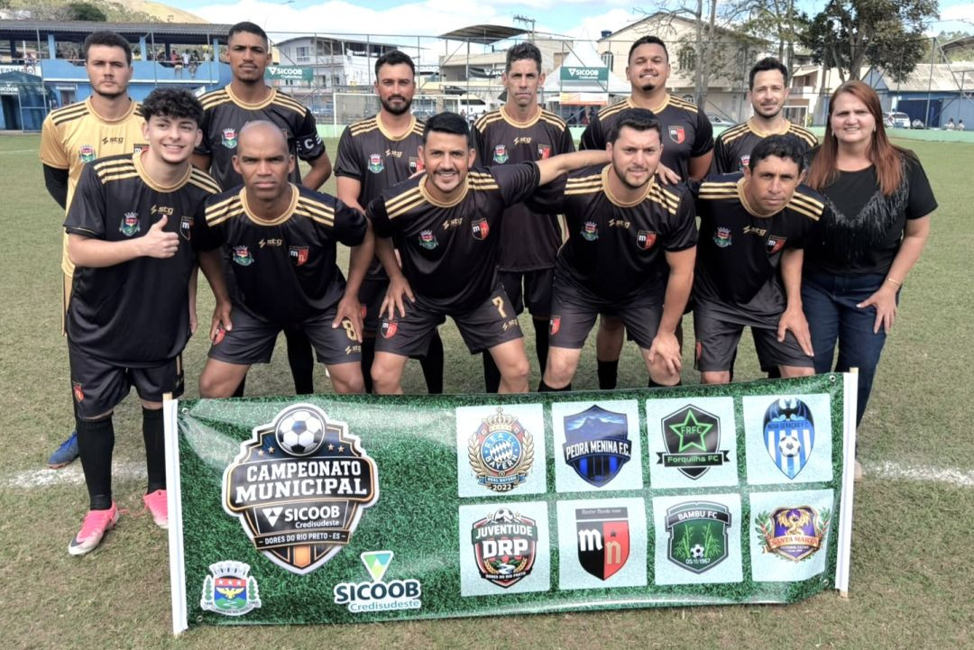 Fotografia do time de futebol amador Mundo Novo posando em pé e ajoelhados no gramado, vestindo uniforme preto e dourado, atrás de uma faixa oficial do Campeonato Municipal de Dores do Rio Preto com os escudos dos clubes participantes.
