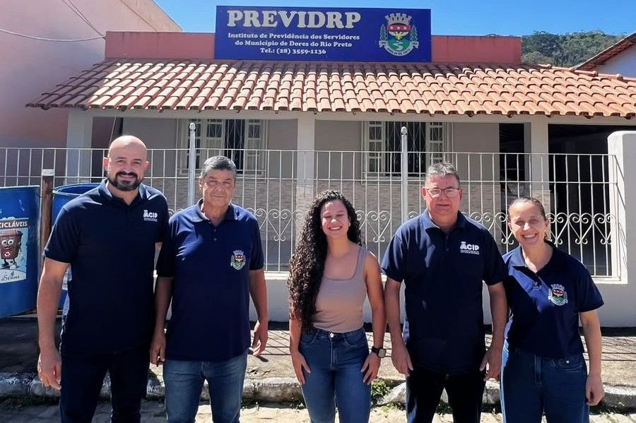 Cinco pessoas alinhadas lado a lado em frente ao prédio do Instituto de Previdência de Dores do Rio Preto (PREVIDRP). O prédio possui fachada clara, portão de ferro e placa azul de identificação.