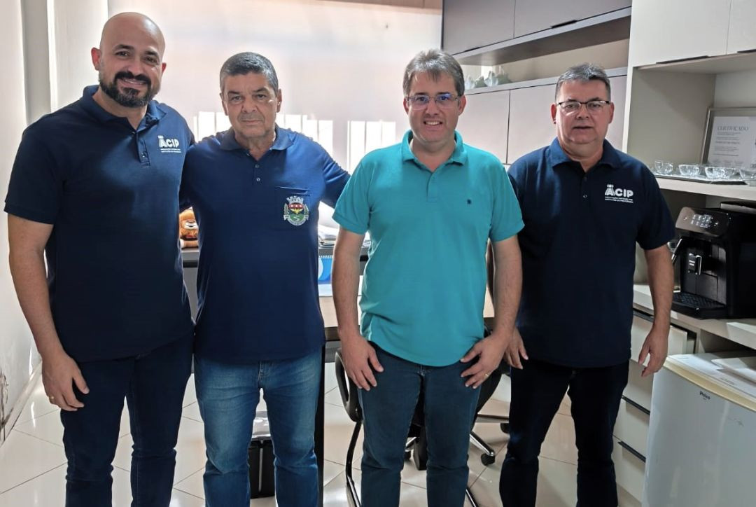 Quatro homens de pé, lado a lado, sorrindo dentro de um escritório. Dois vestem camisas polo azuis da ACIP-ES e o prefeito vestindo camisa polo verde clara está ao centro.